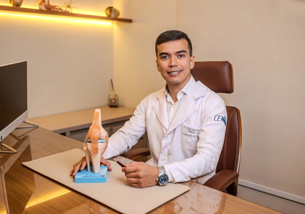 Dr. Frank Sampaio de jaleco com um modelo anatômico do joelho